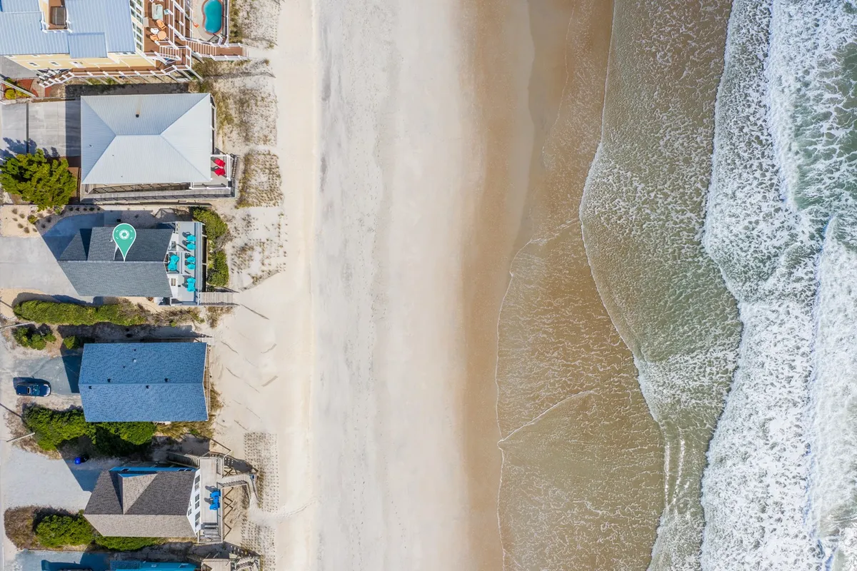 A wide-angle exterior photo shows beachfront properties with sandy shores and the rolling ocean waves just beyond, with clear access to the beach for easy family outings. There are visible pathways leading directly to the sand, ideal for beach games, swimming, and sandcastle building.