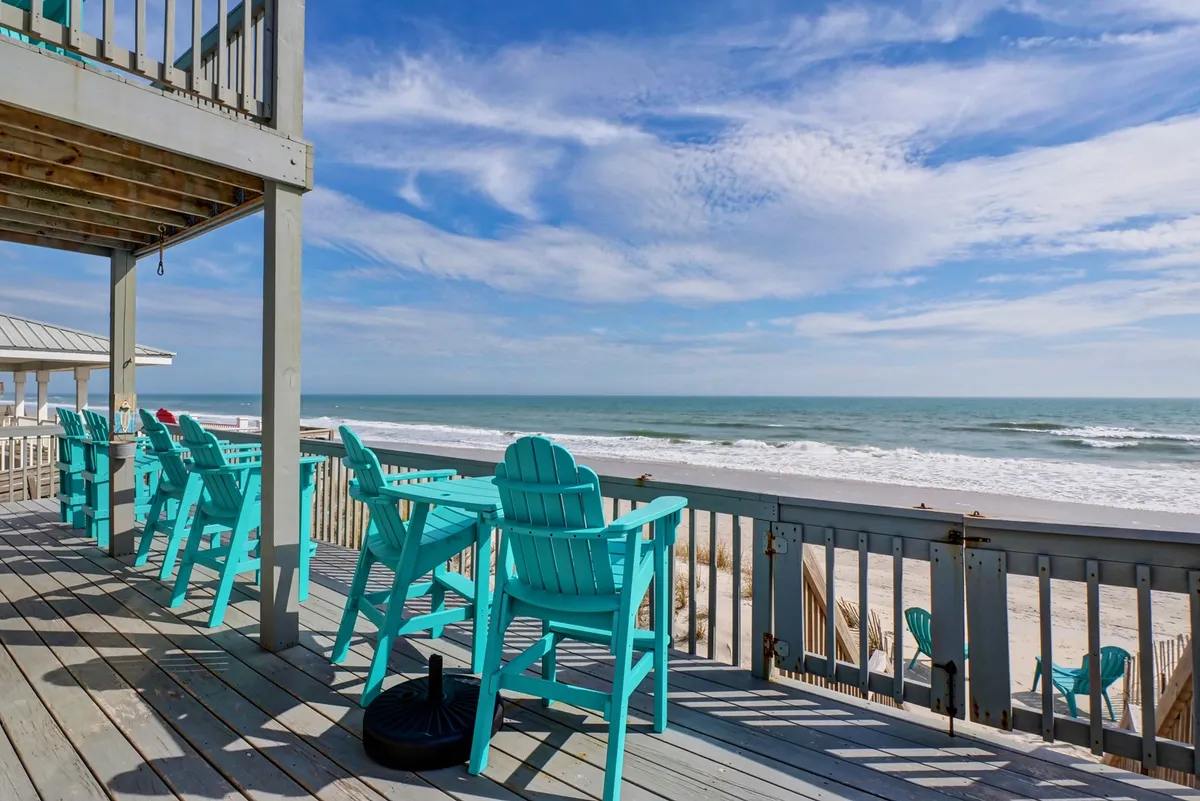 The hero image showcases a sun-kissed deck overlooking the ocean, furnished with inviting turquoise chairs that invite relaxation while basking in the serene coastal breeze. The deck's railing frames a stunning, unobstructed view of the waves, creating an idyllic spot for sunset cocktails or dolphin watching.